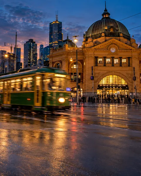 A green tram passing Flinders Street Station at dusk