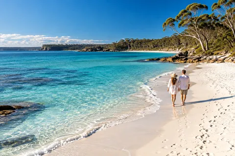 A couple walking a white-sand beach beside turquoise water